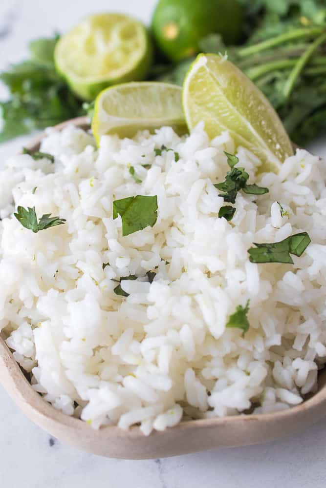 vertical close up shot of cilantro rice with limes and topped with chopped cilantro