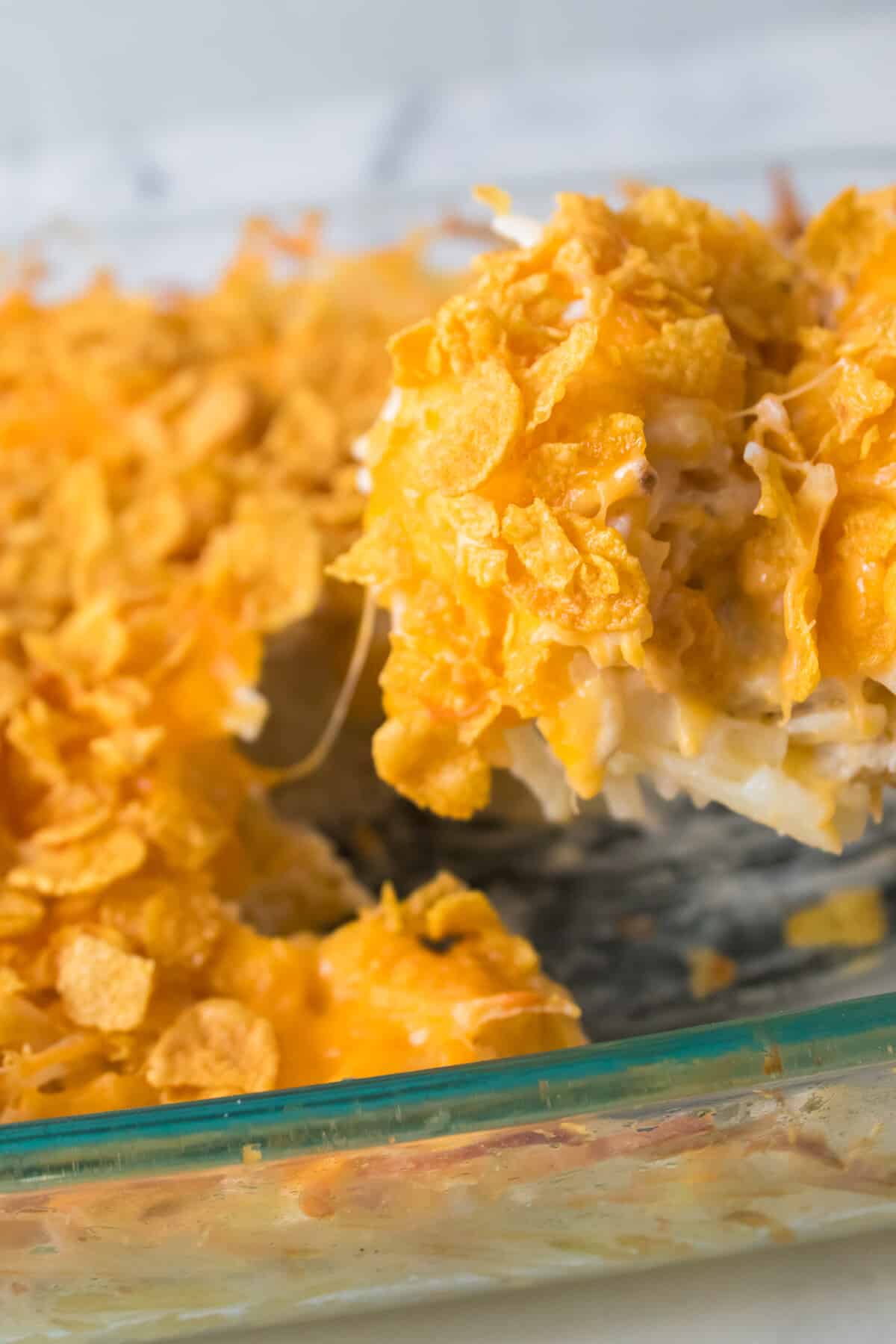 spoon scooping out funeral potatoes from glass casserole dish