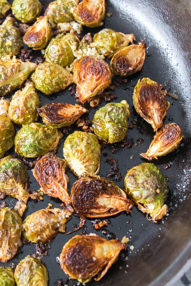 roasted brussel sprouts topped with salt, pepper and minced garlic in cast iron skillet