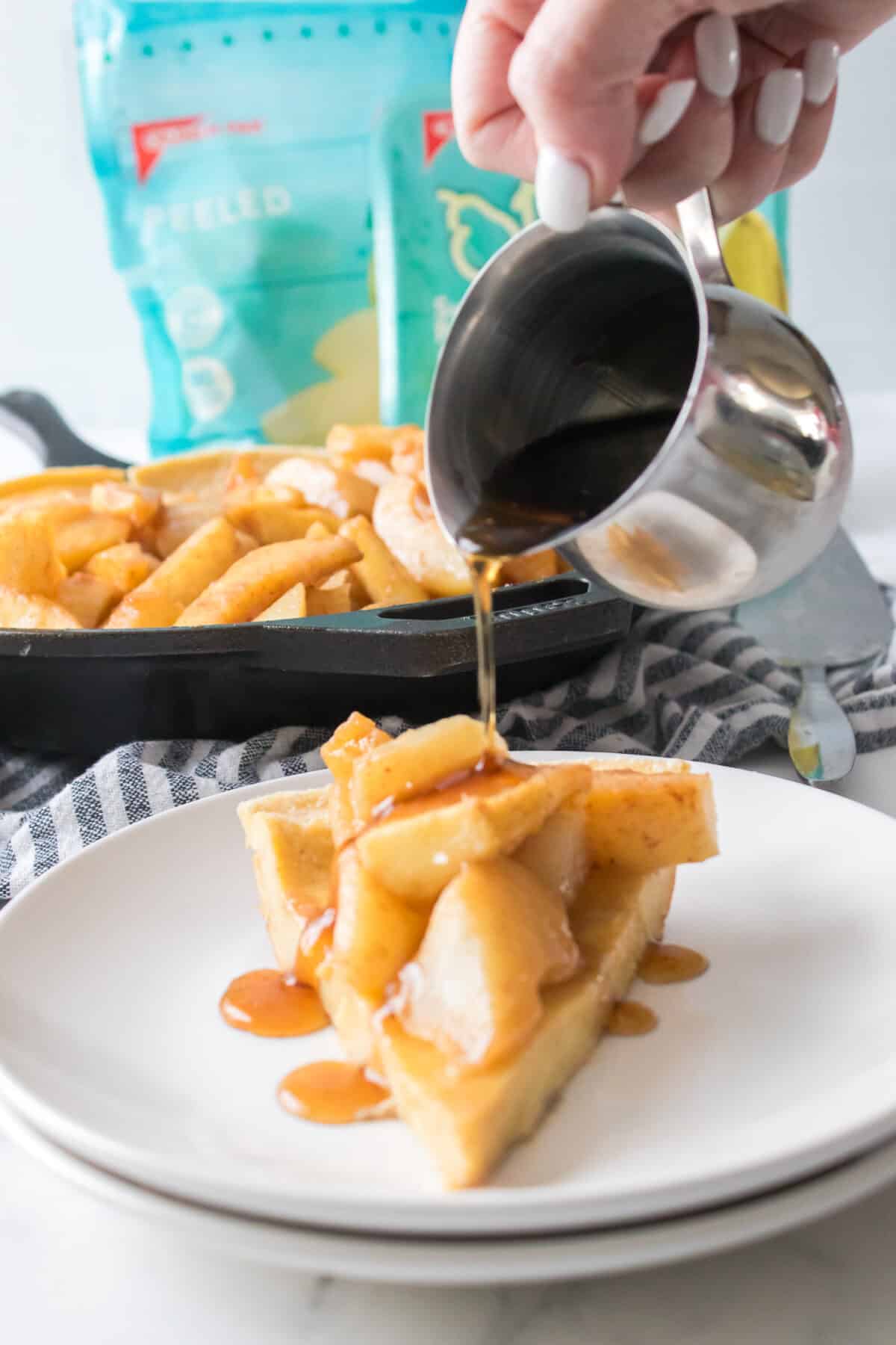hand pouring syrup over puff pancake topped with caramelized apples and pears