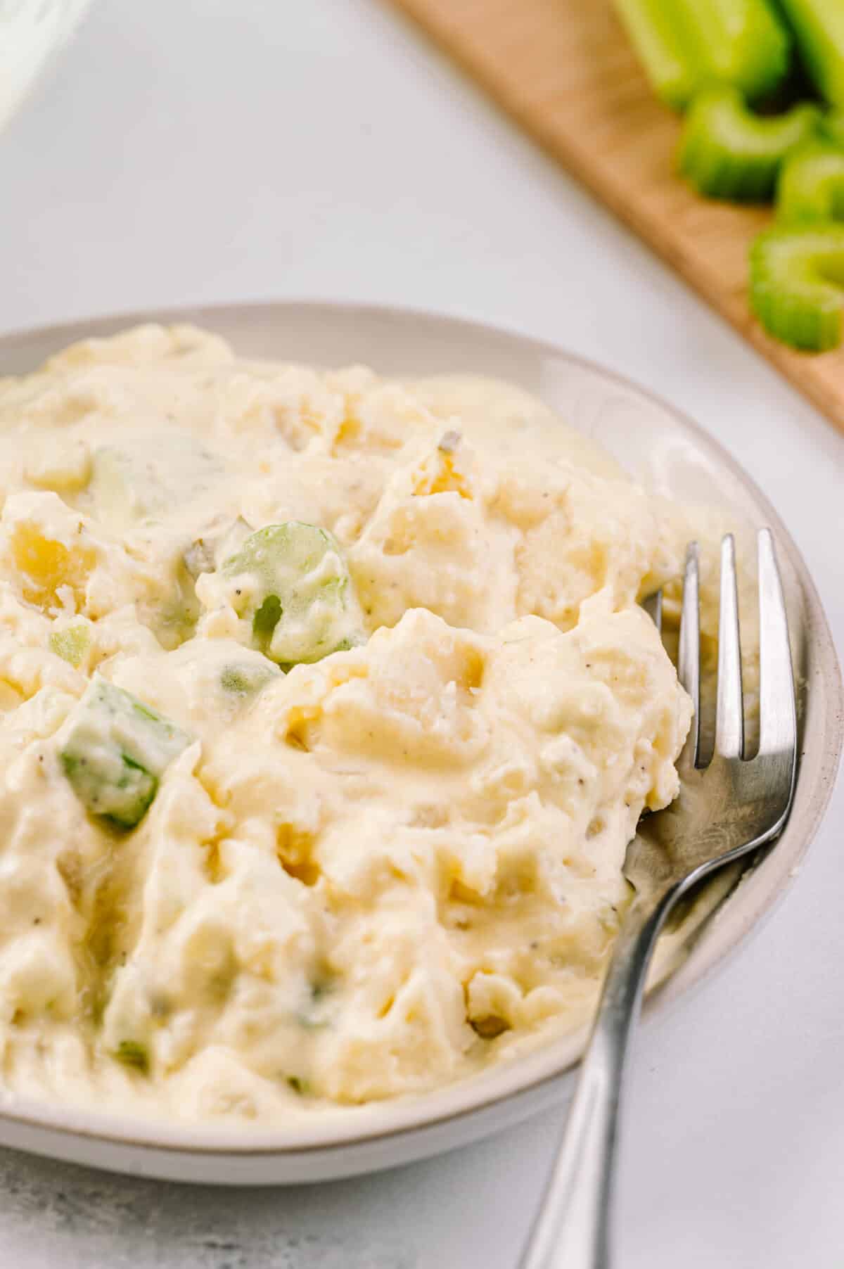 close up vertical shot of potato salad in serving bowl with fork