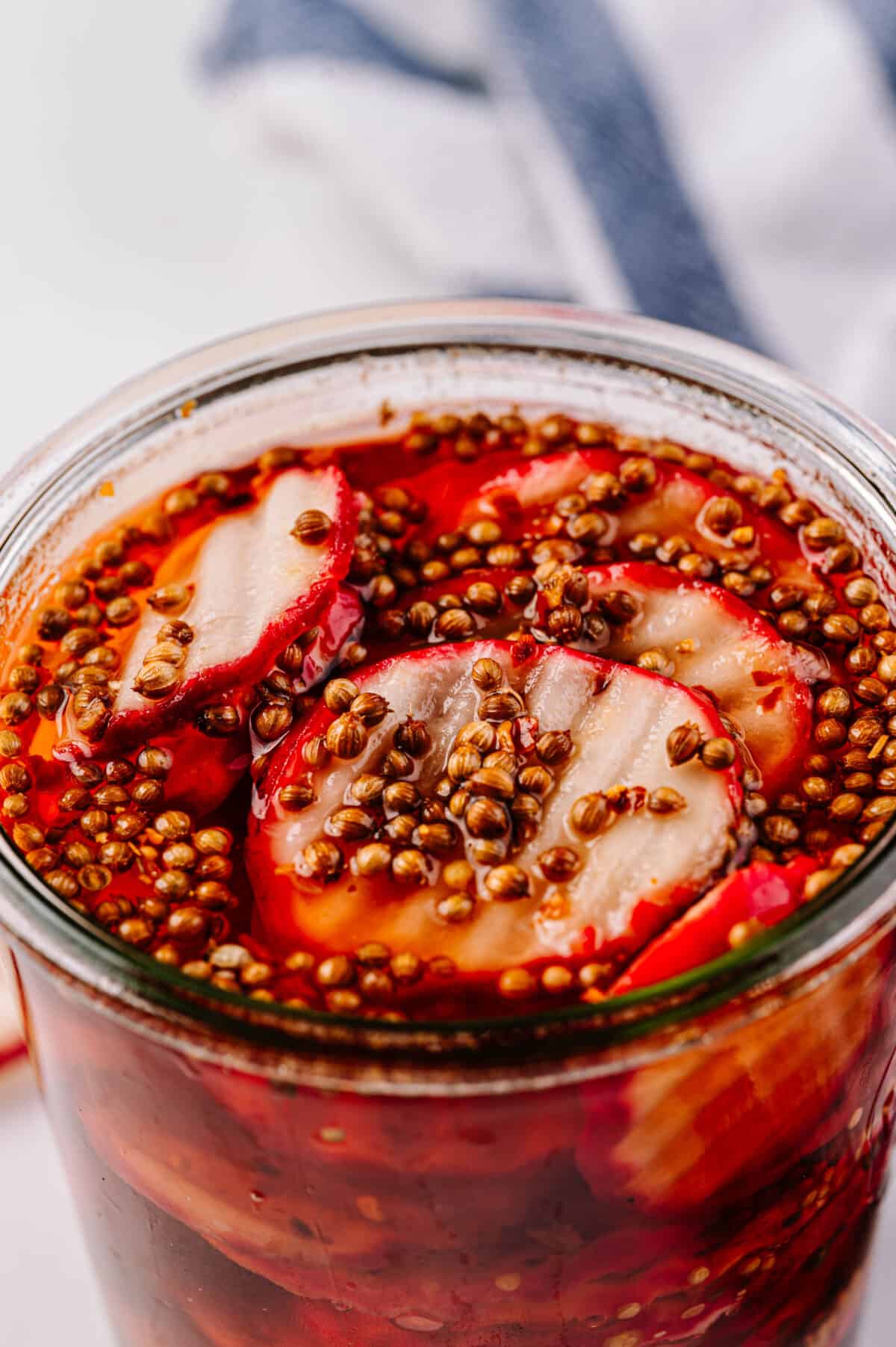 close up vertical shot of pickled radishes with radish coins in glass jar