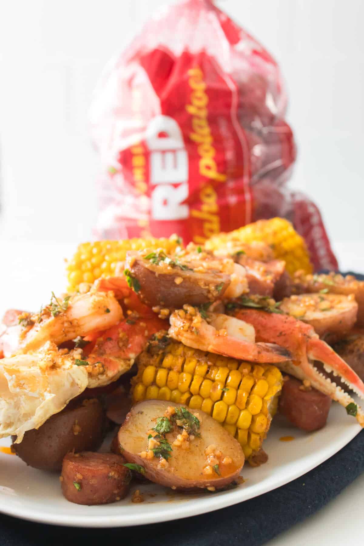 seafood boil on white serving platter with bag of wada farms red potatoes in background