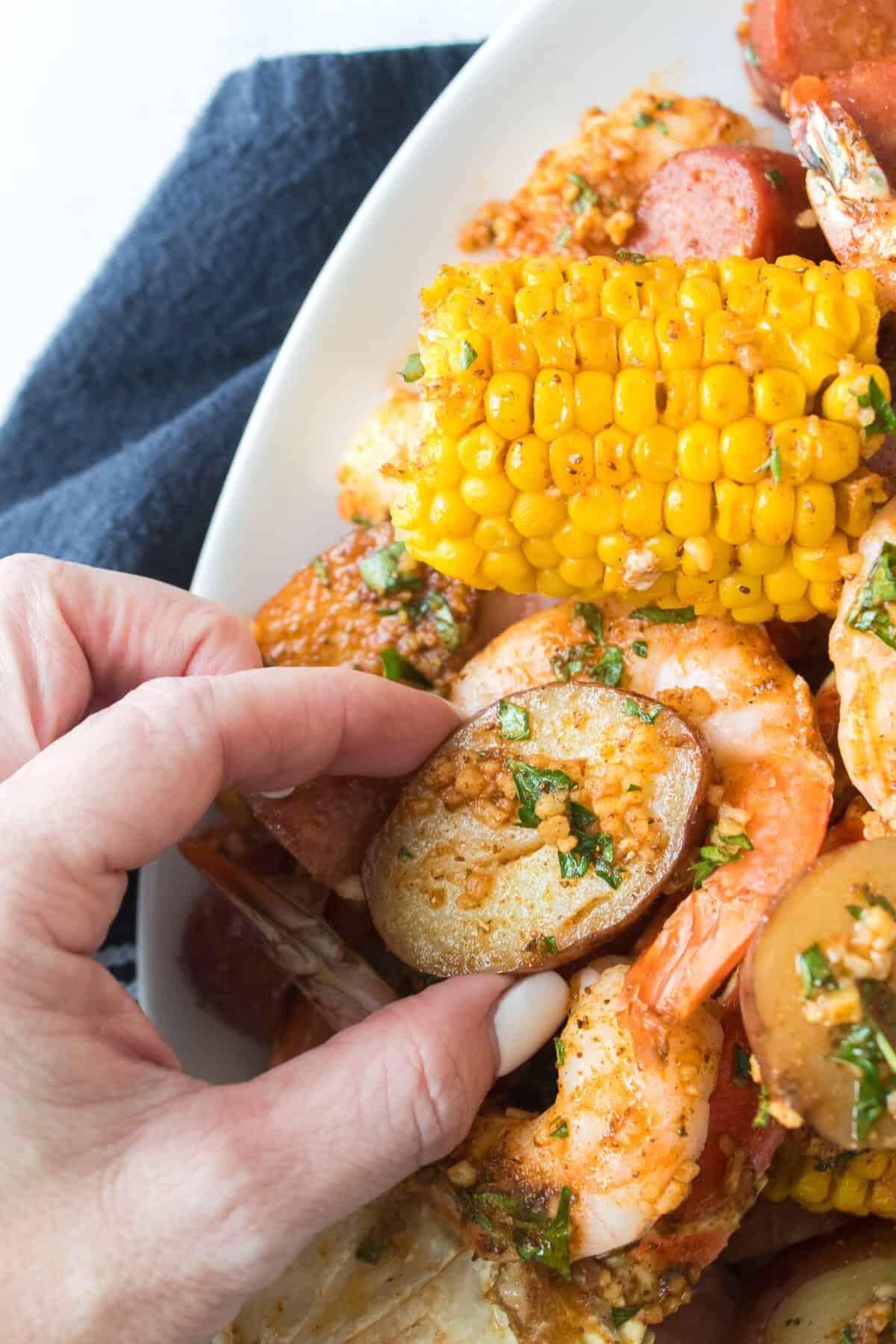 hand grabbing red potato from plate of seafood boil