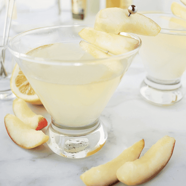 Two apple martinis in clear glasses surrounded by apple slices