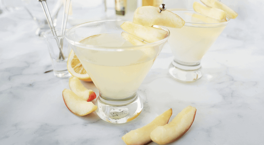 Two apple martinis in clear glasses surrounded by apple slices