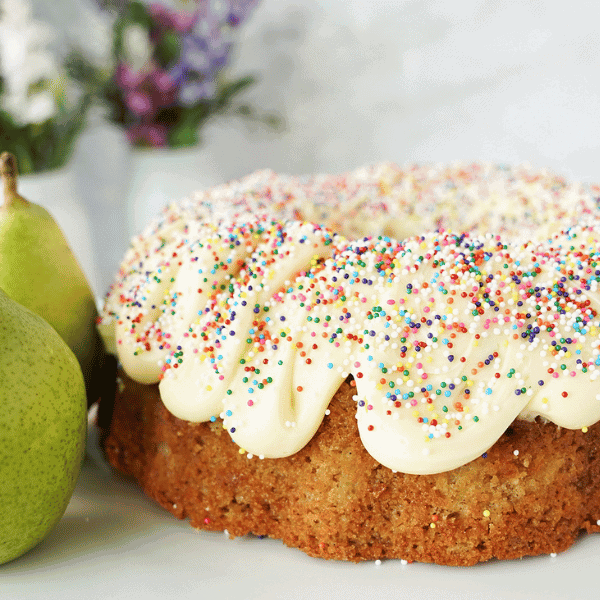 Whole Pear Bundt Cake on white stand with green amjou pears
