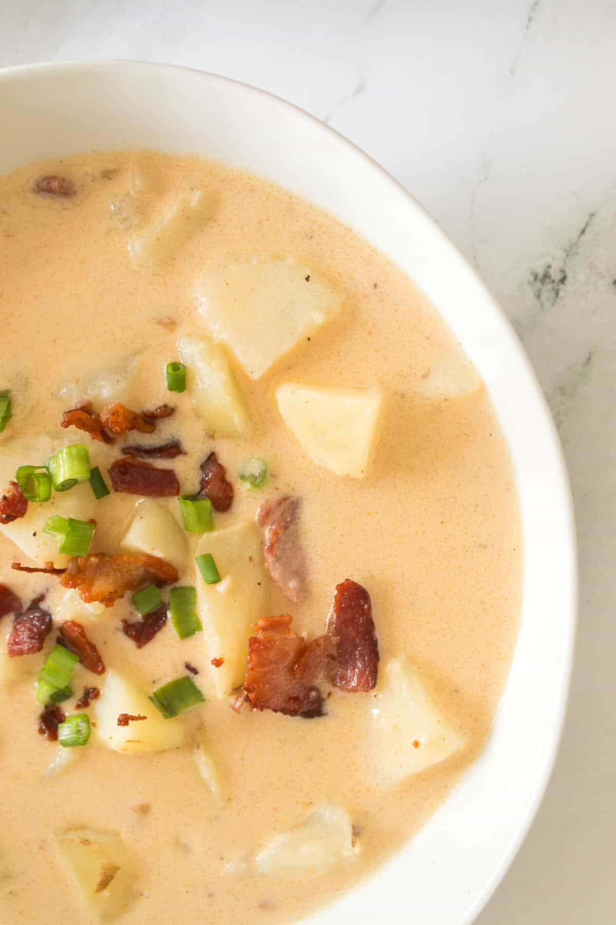 vertical close up shot of loaded potato soup topped with green onions and bacon in bowl