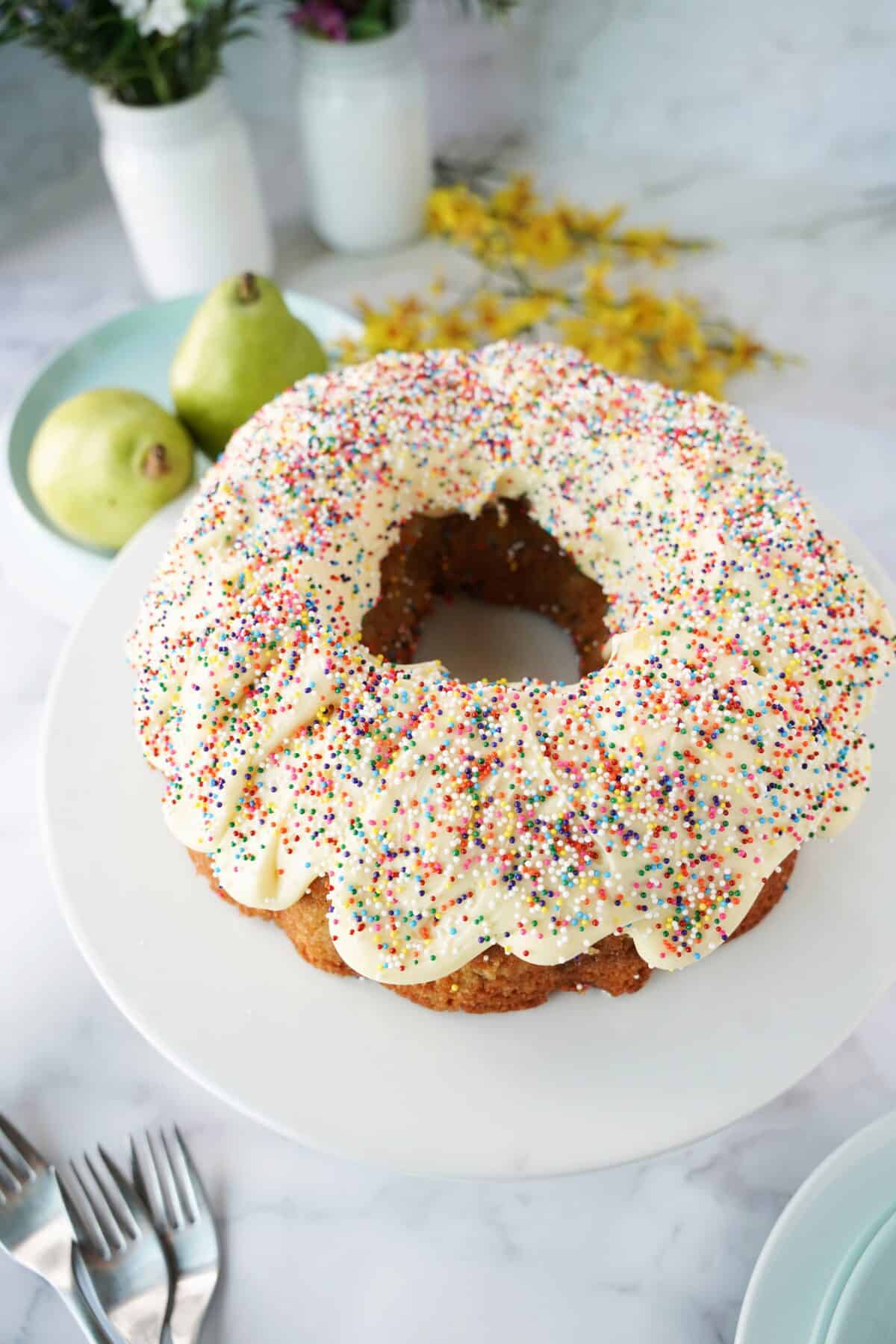 vertical 45° shot of pear bundt cake on serving platter topped with buttercream frosting and sprinkles