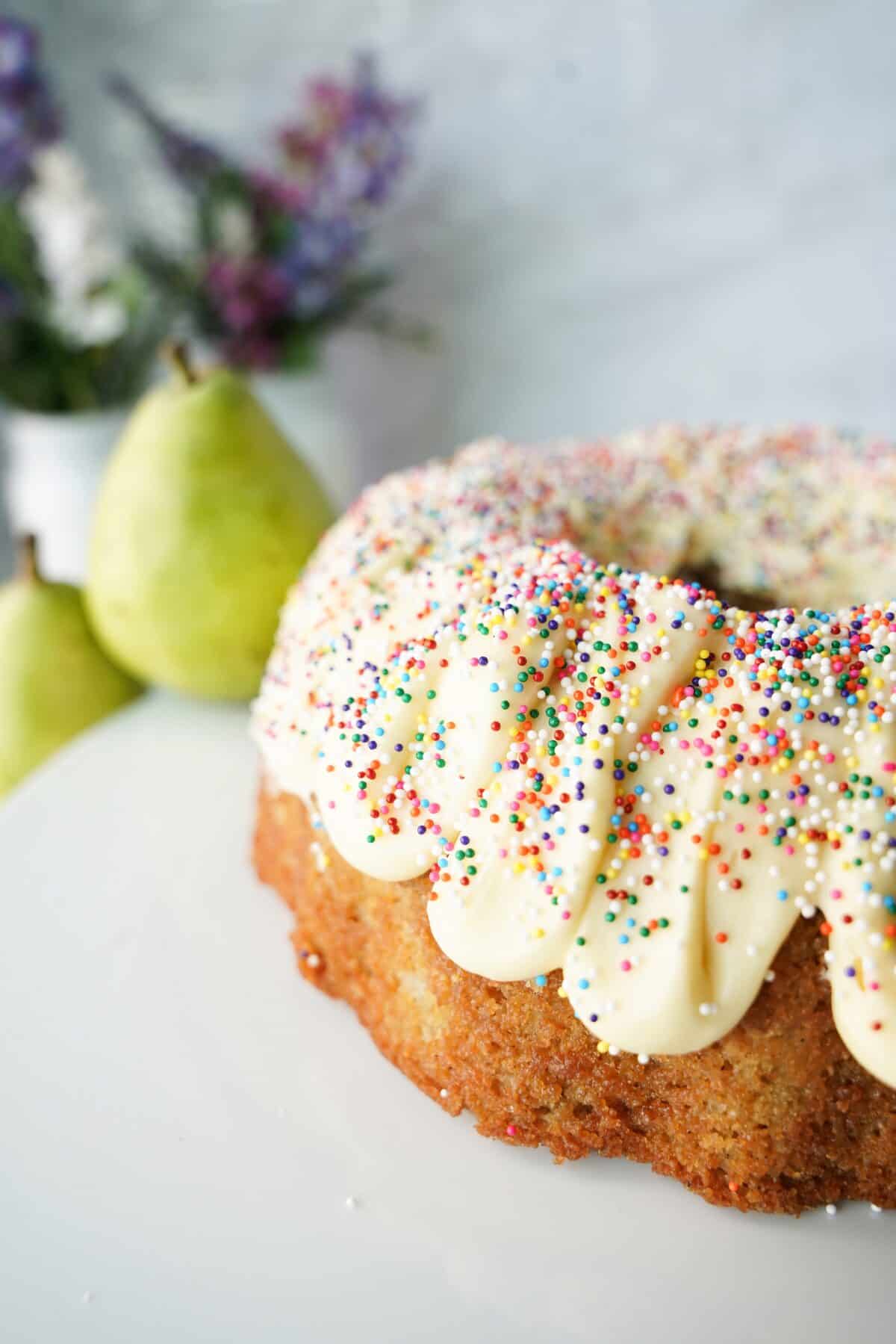 vertical head on close up shot of pear bundt cake with buttercream frosting and sprinkles