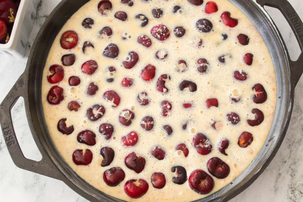 cast iron skillet with cherries on bottom with clafoutis batter poured over the time prior to baking