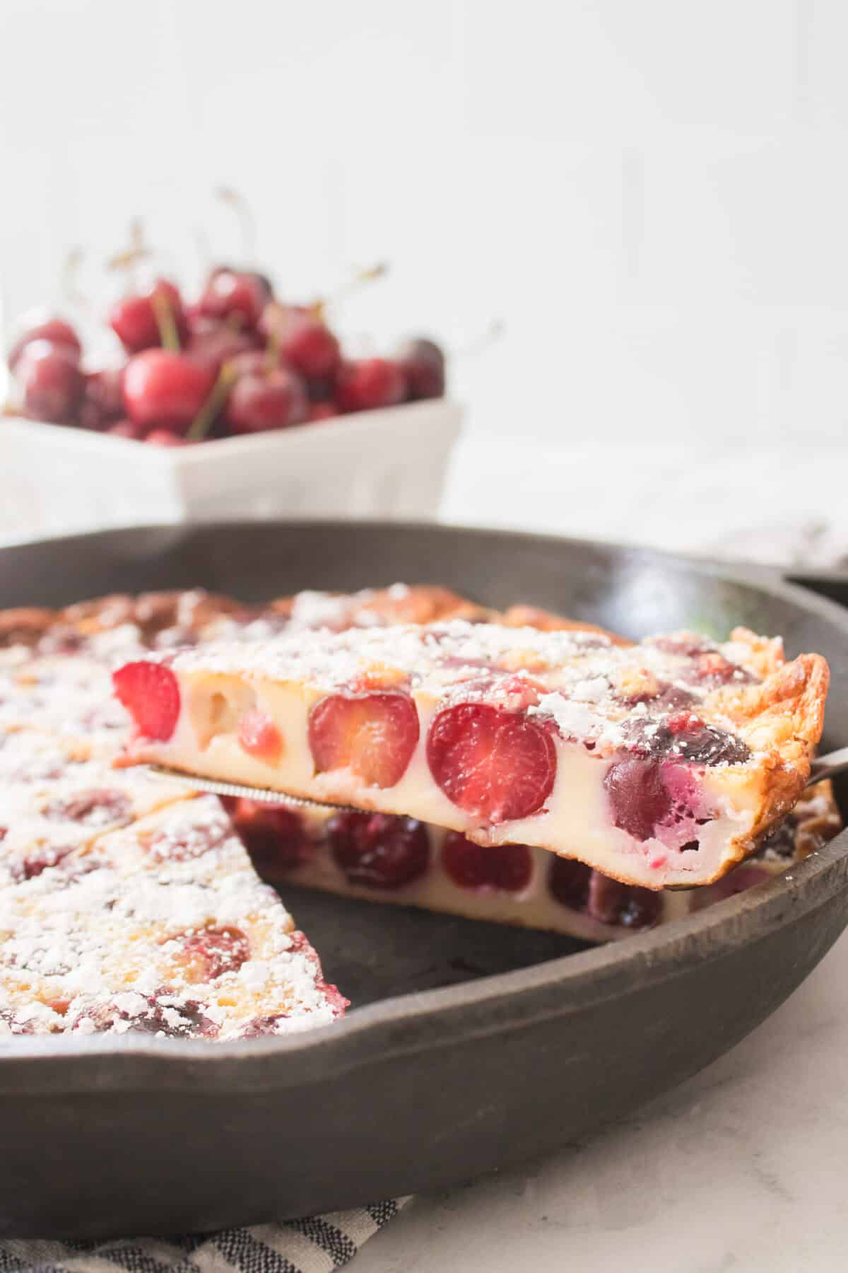 slice of cherry clafoutis being taken out of cast iron skillet