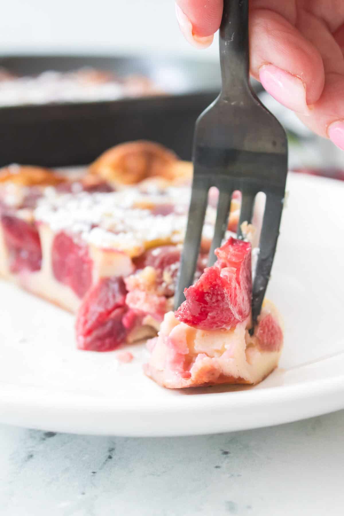 hand holding a fork taking a bite out of cherry clafoutis