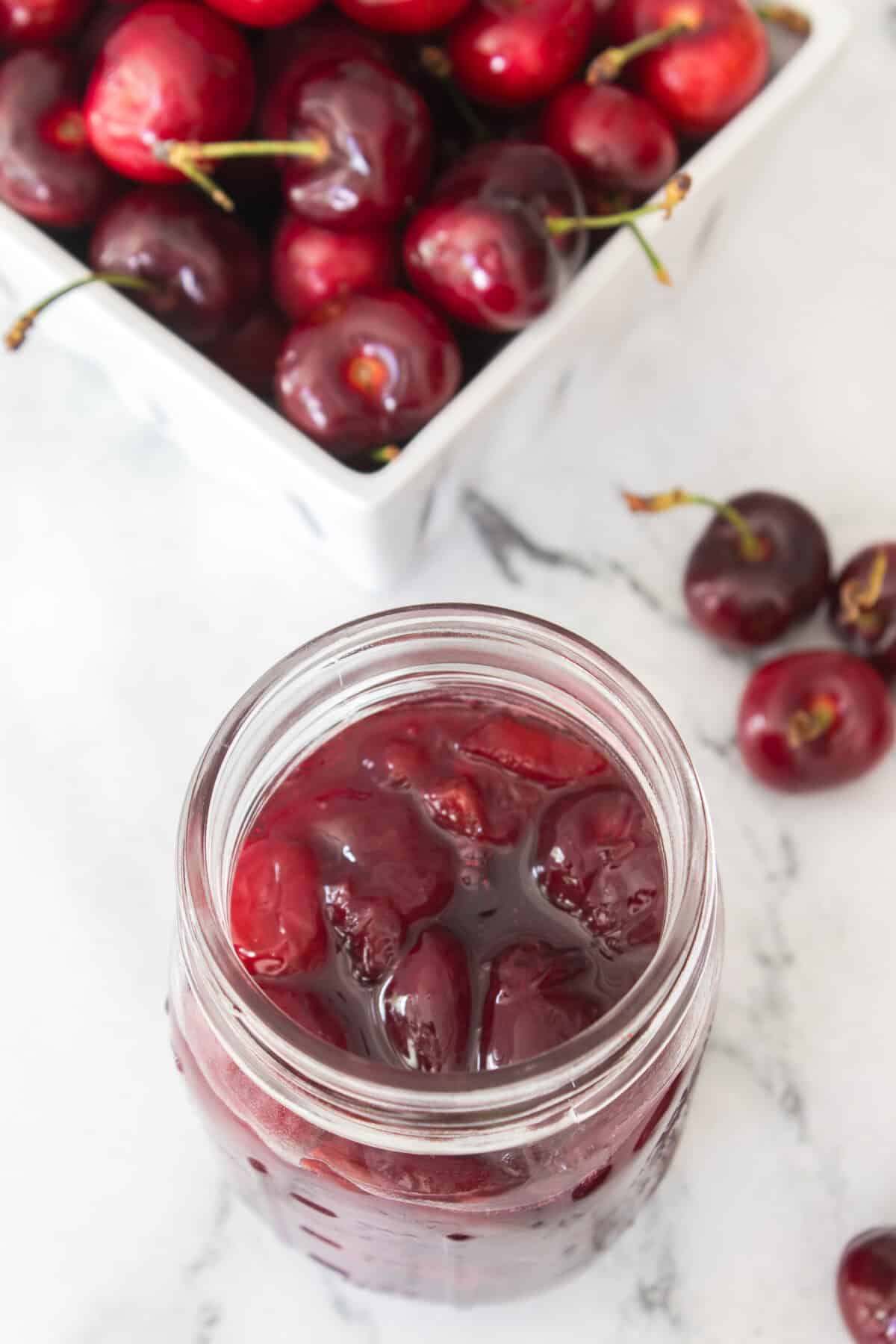 cherry pie filling in mason jar with bowl of fresh sweet cherries in background