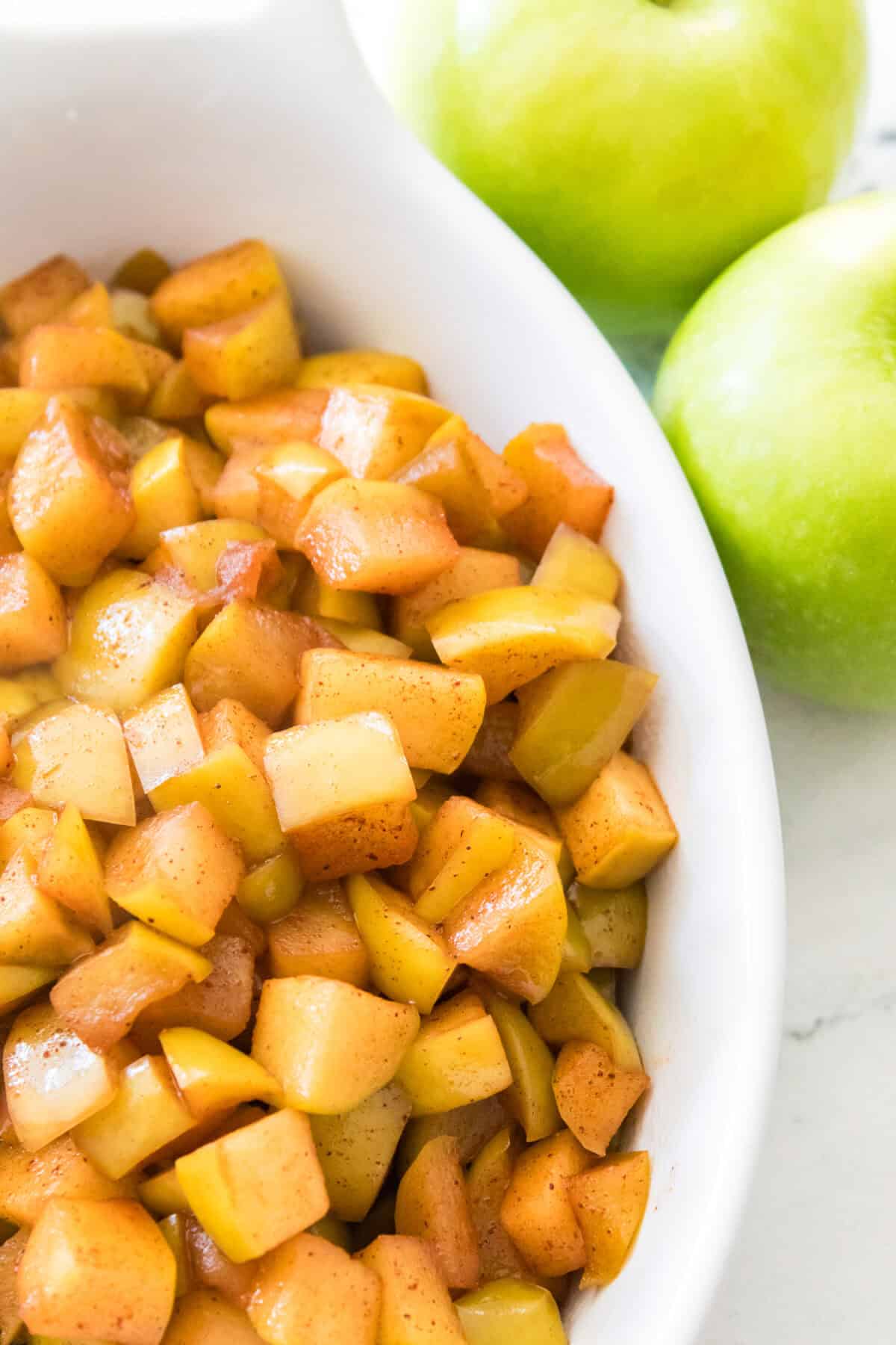 close up vertical shot of warm cinnamon apples in white serving dish
