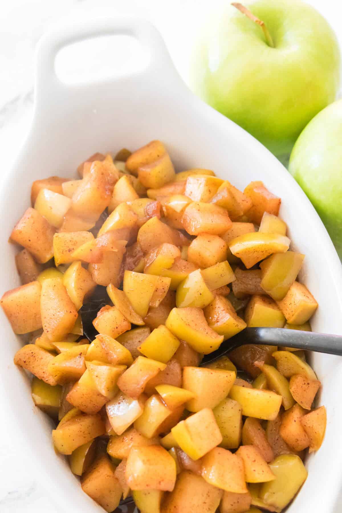 white serving dish with warm steamy cinnamon apples with spoon for serving