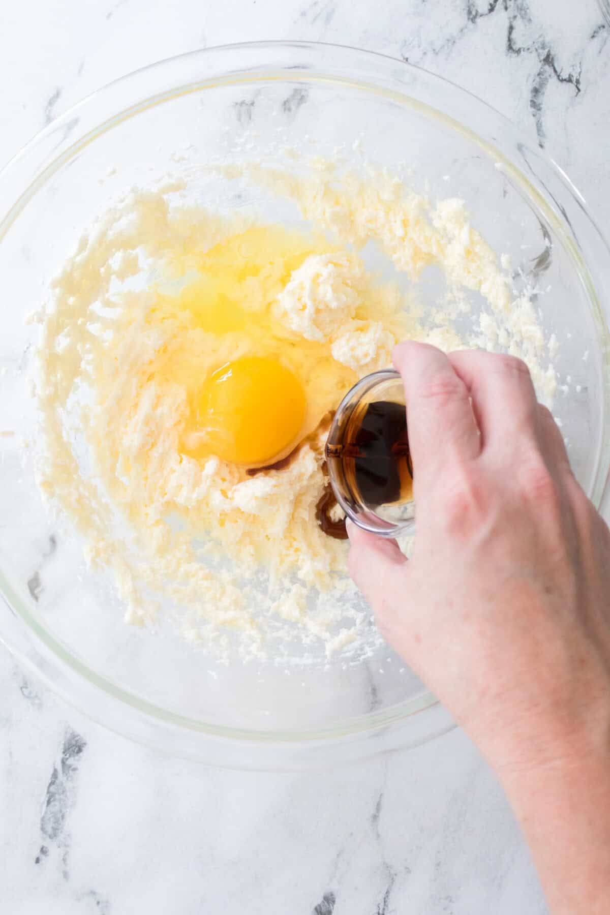 butter and sugar creamed together with egg in bowl and a hand pouring in vanilla extract