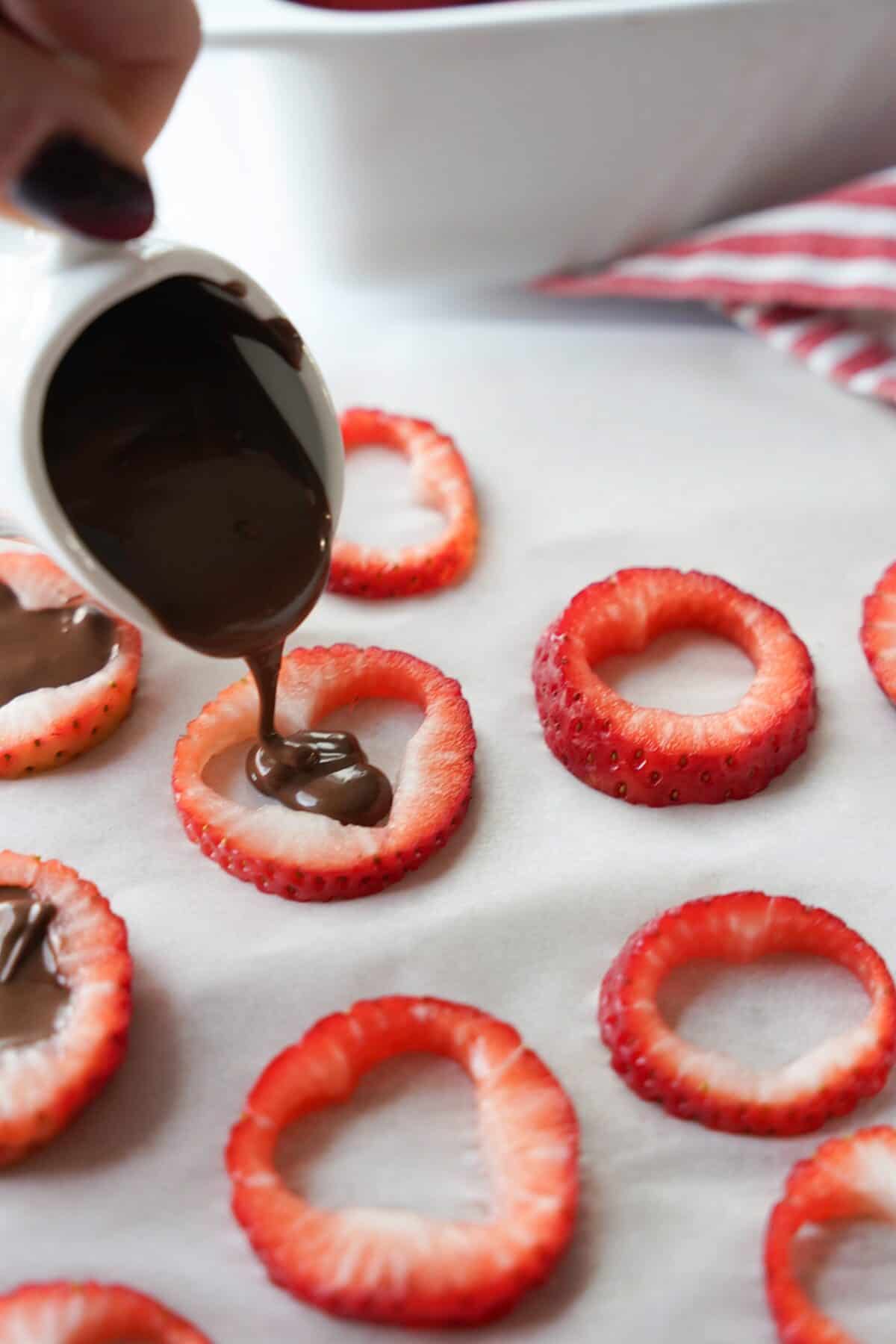 hand pouring melted chocolate into sliced strawberry cut out in a shape of a heart