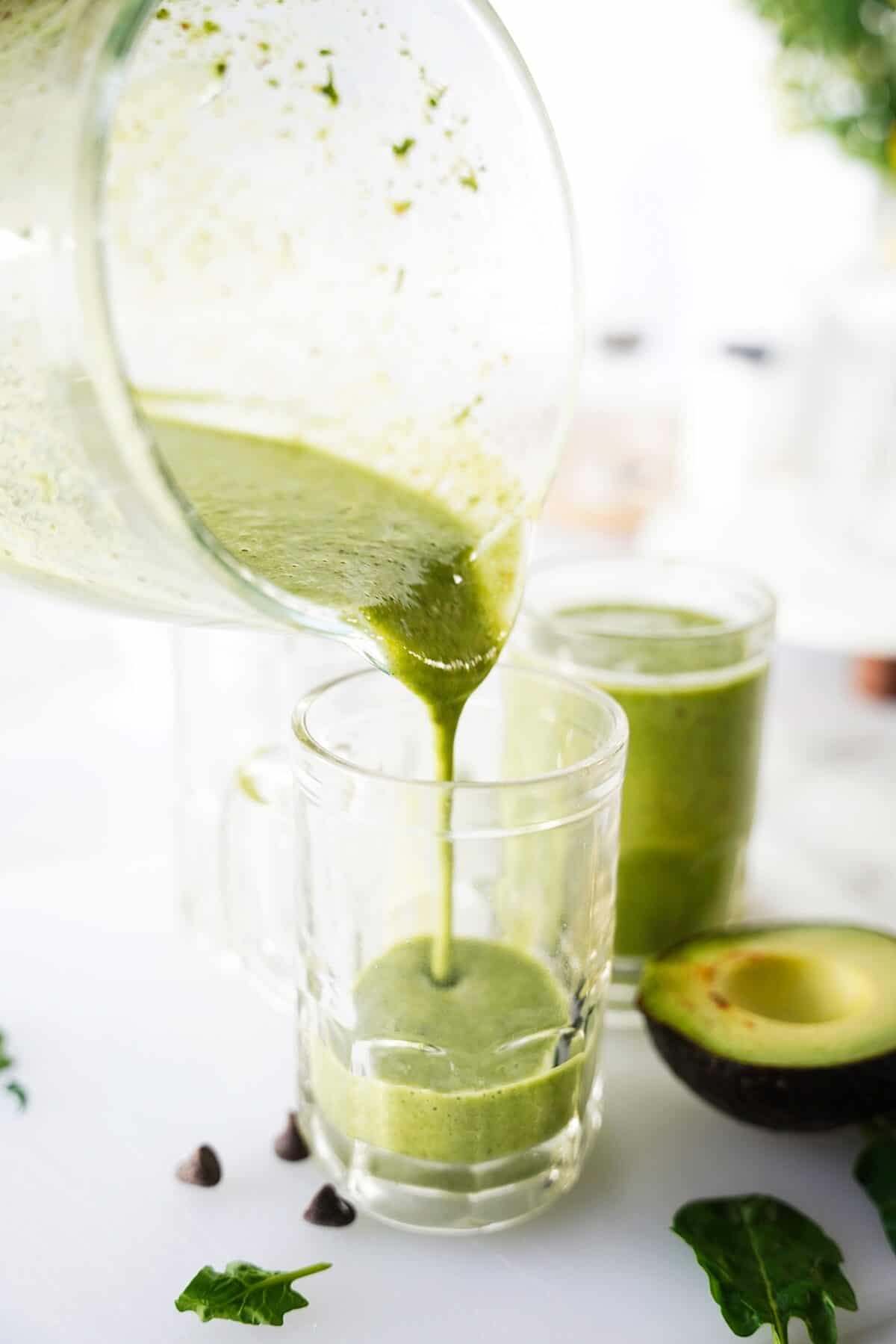 avocado smoothie being poured from blender into a glass mug