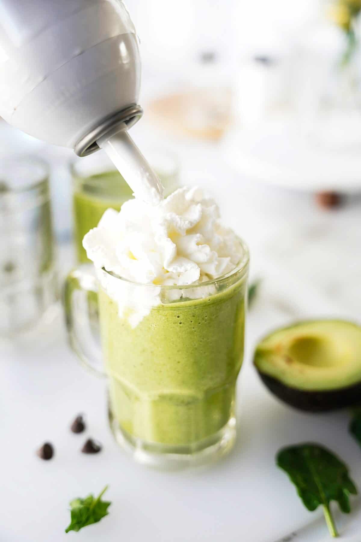 can of whipped cream on top of glass mug with green smoothie