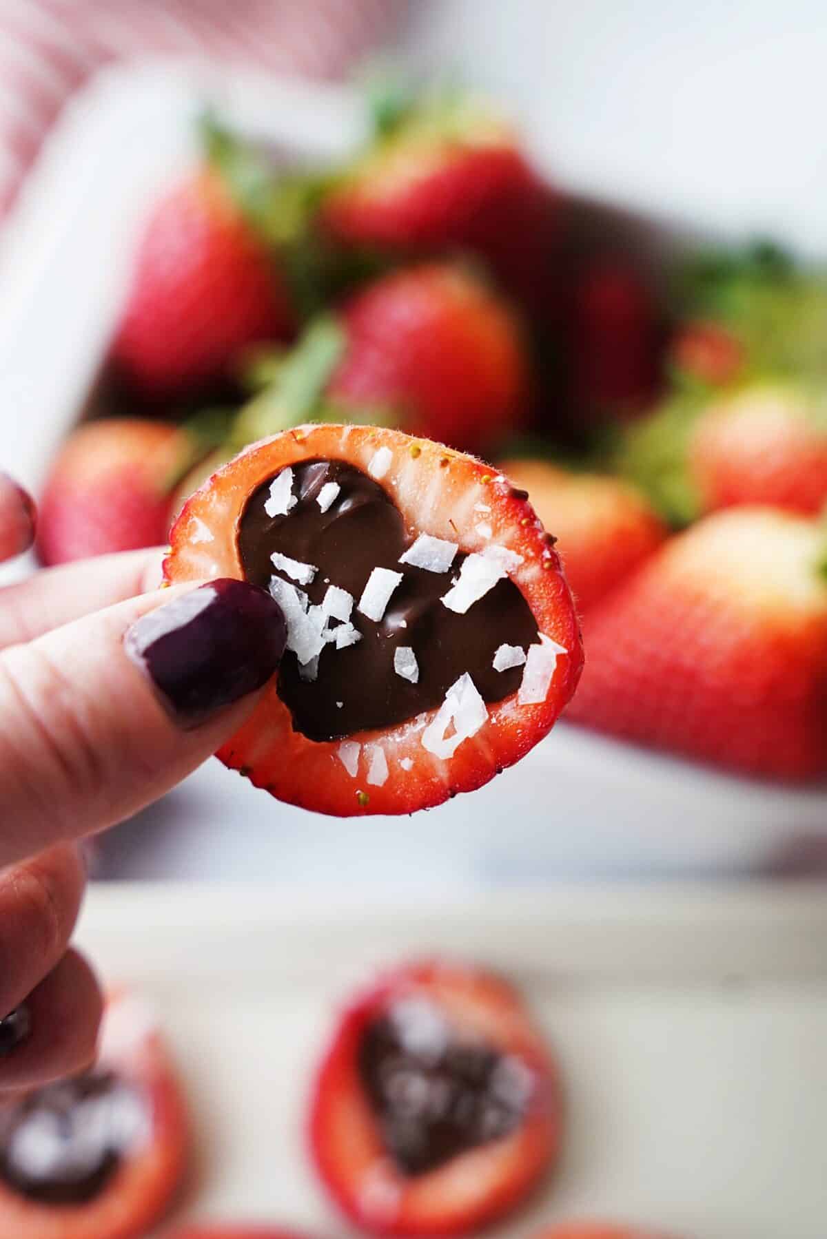 hand holding sliced strawberry cut out with hardened chocolate topped with chopped coconut flakes