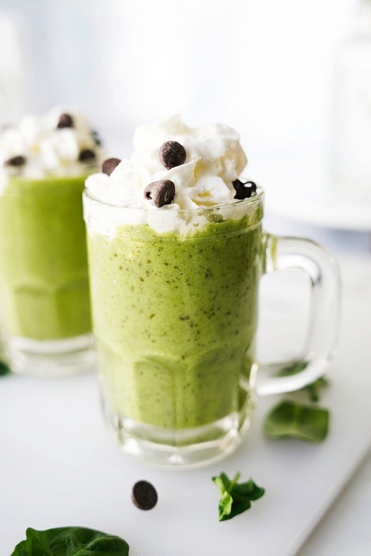head on shot of avocado green mint smoothie in glass mug topped with whipped cream and chocolate chips