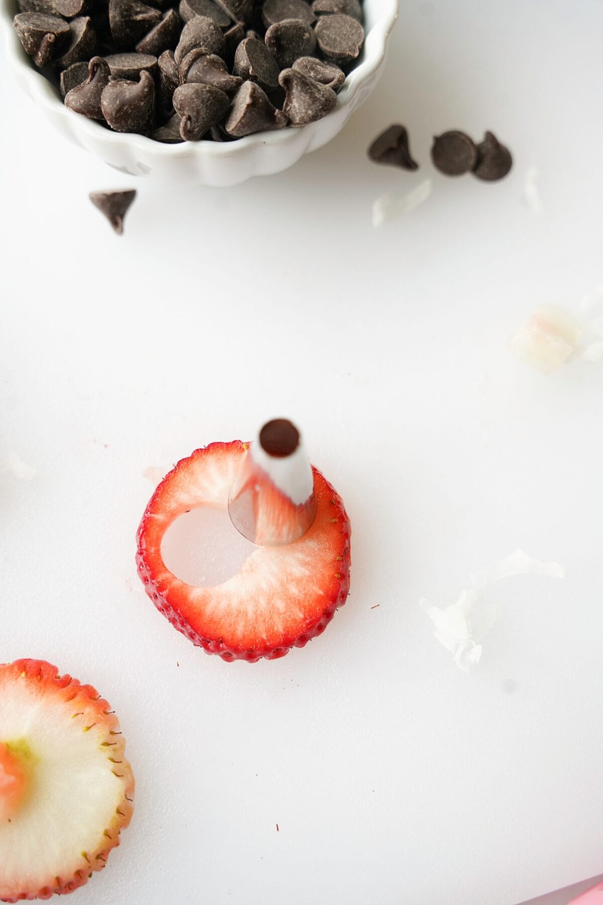 overhead shot of icing tip cutting small holes in a sliced strawberry for the round part of a heart