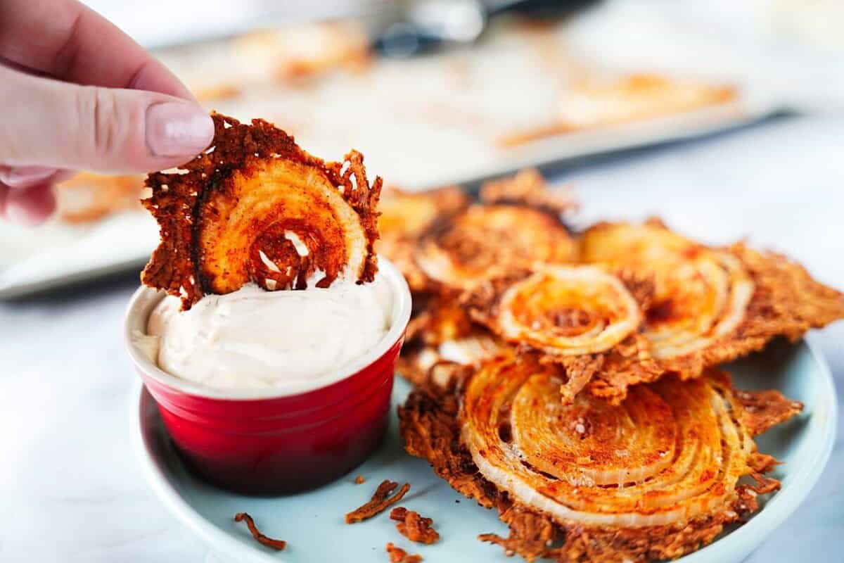 Dipping a single onion chip in dip with plate of onion chips