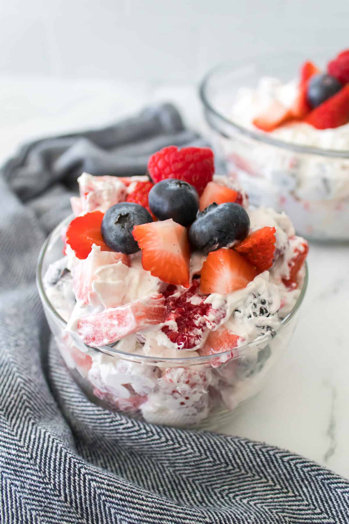 close up vertical shot of summertime cheesecake fruit salad topped with blueberries, strawberries and raspberries