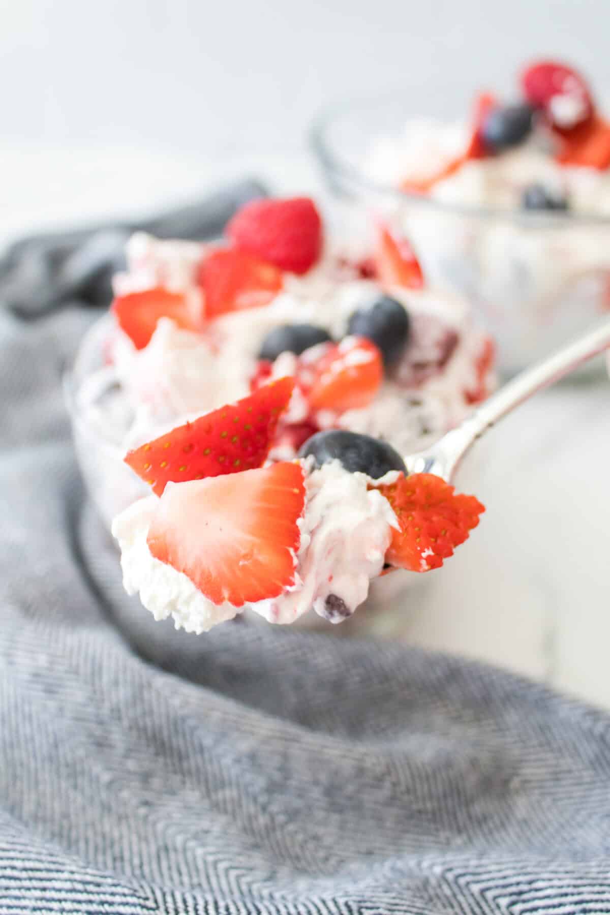 close up vertical shot of summertime cheesecake fruit salad on spoon