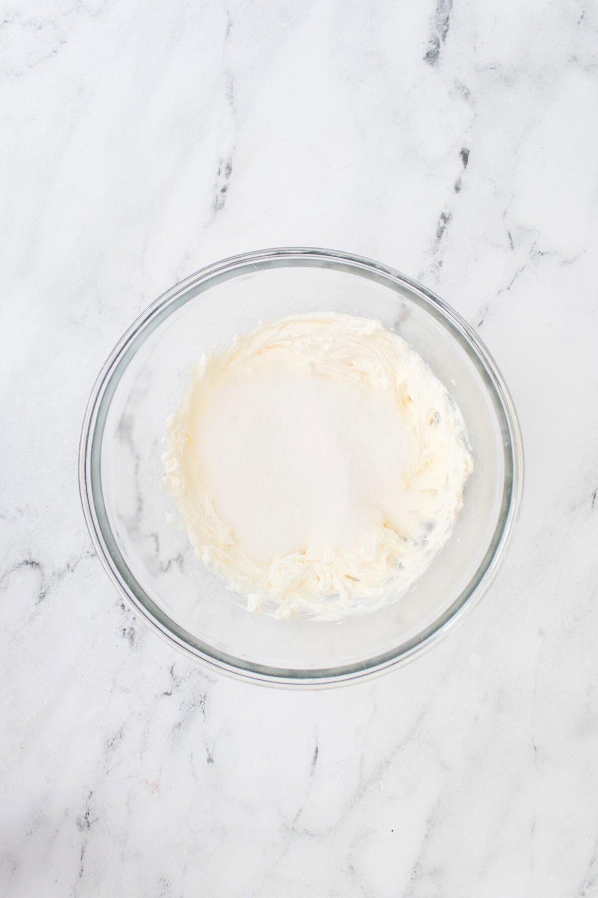 glass bowl with creamy cream cheese and sugar being added