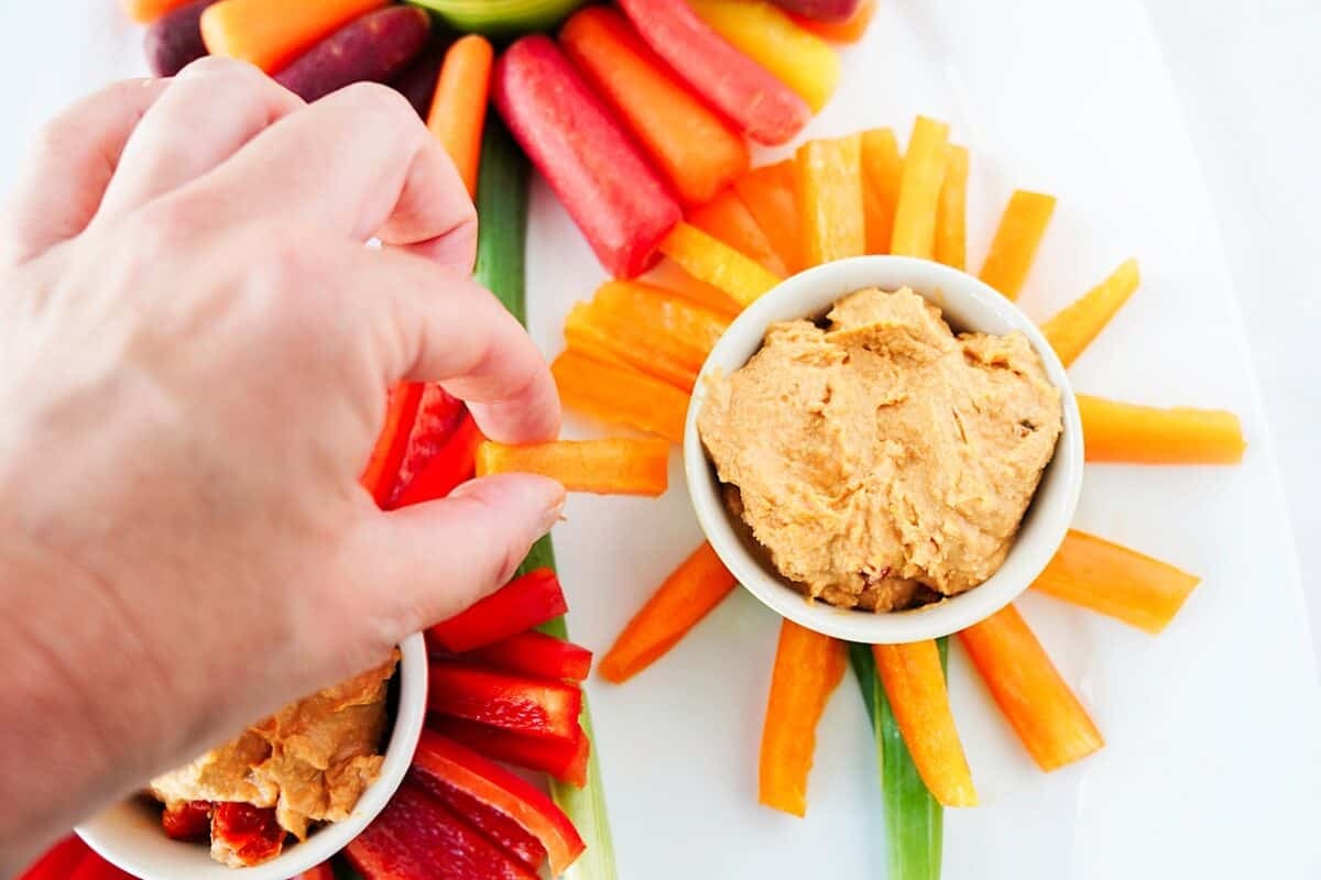 overhead shot of hand placing cut bell peppers on serving platter around a bowl of hummus to create a flower