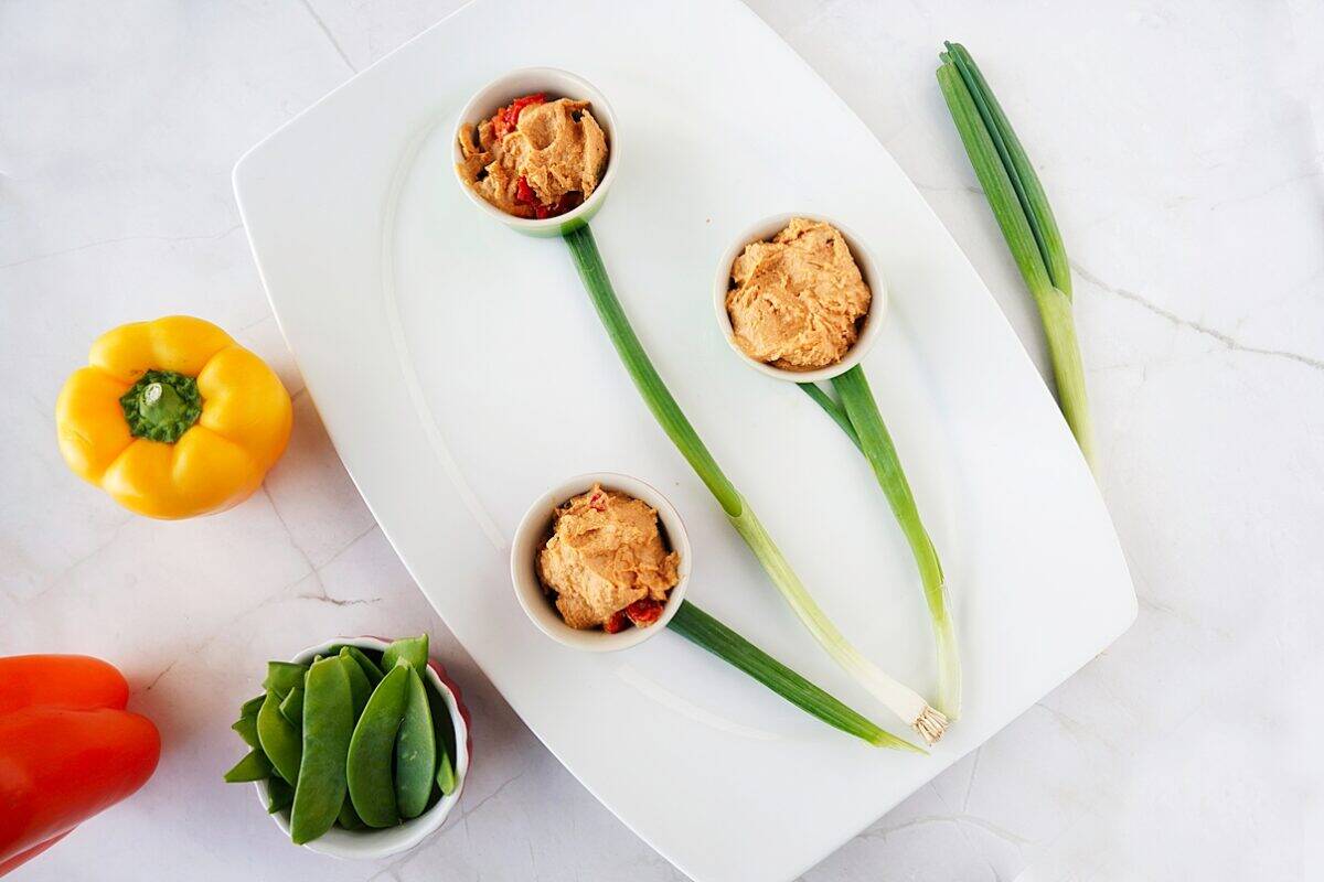 overhead shot of 3 bowls of hummus on tray, with stems of green onions
