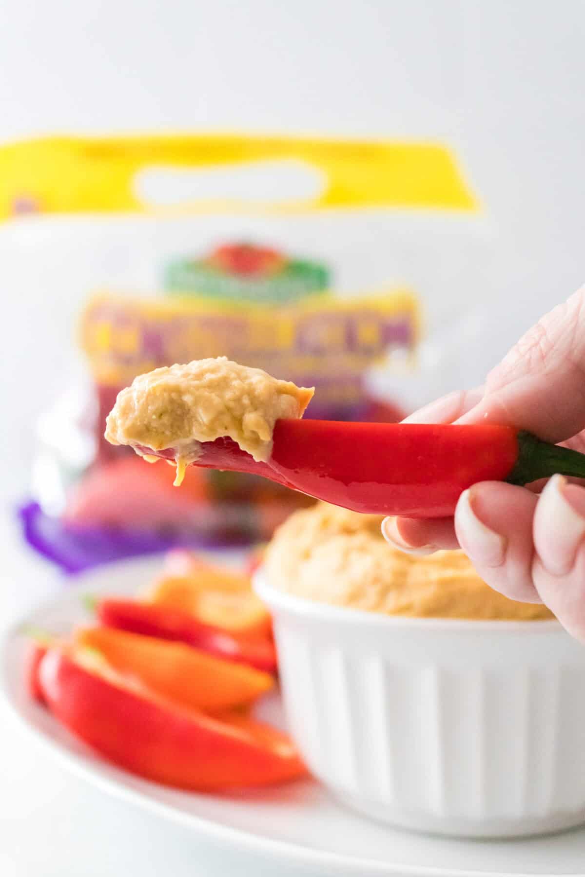 hand holding red mini pepper dipped in roasted pepper hummus