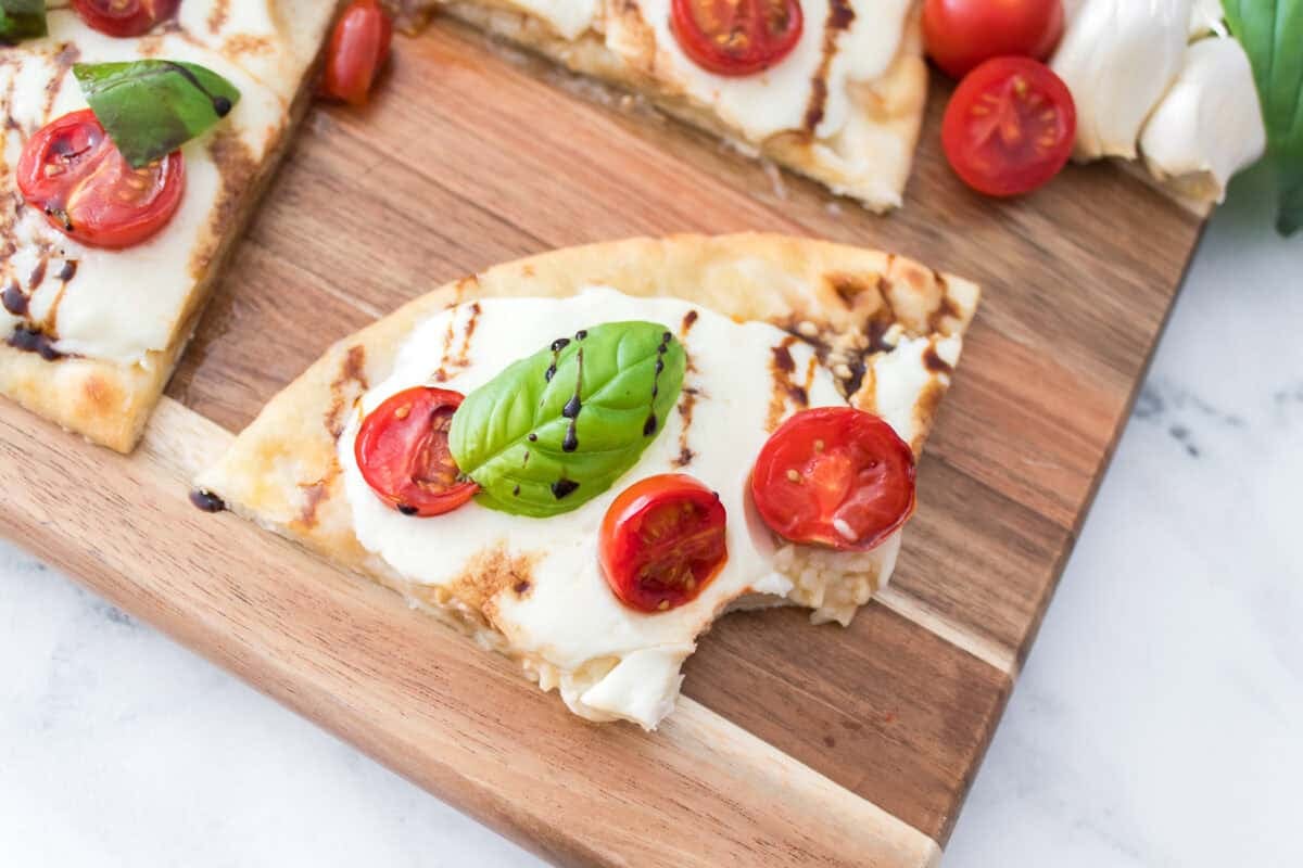 bite taken out of caprese flatbread sitting on cutting board