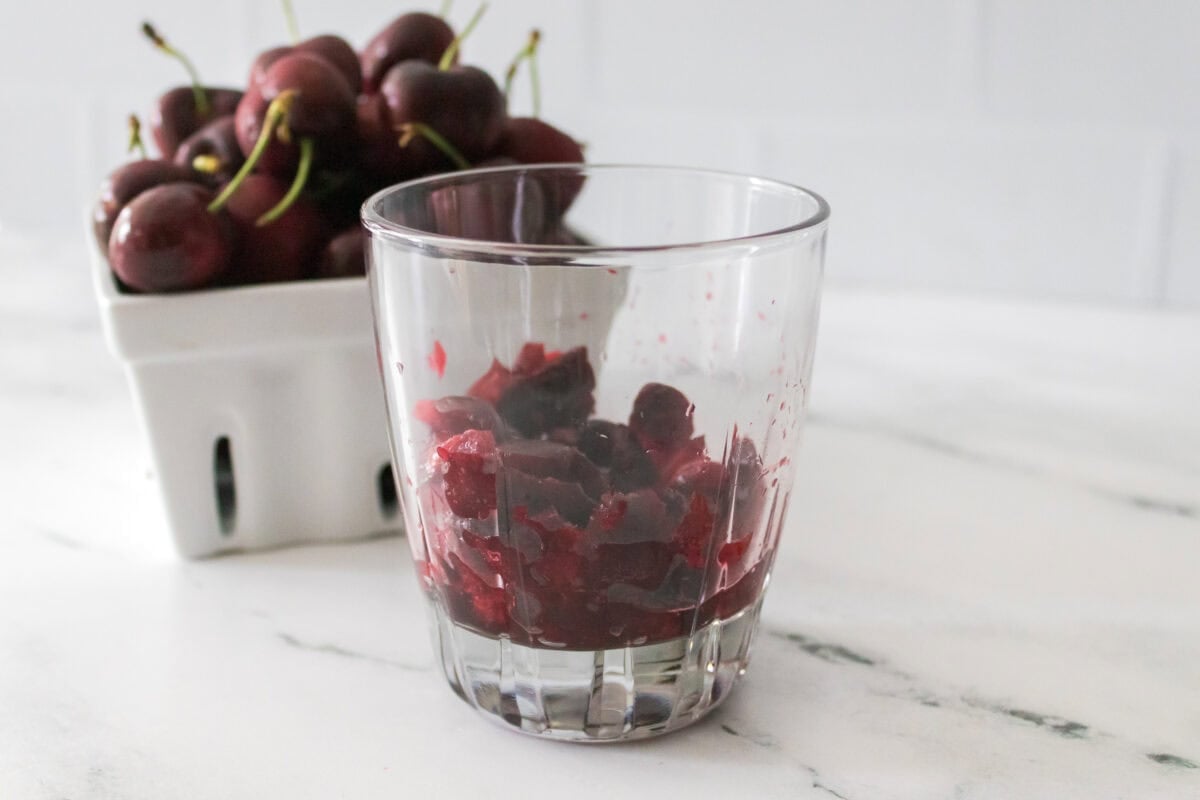 cherries in glass jar after being muddled with bowl of cherries in background