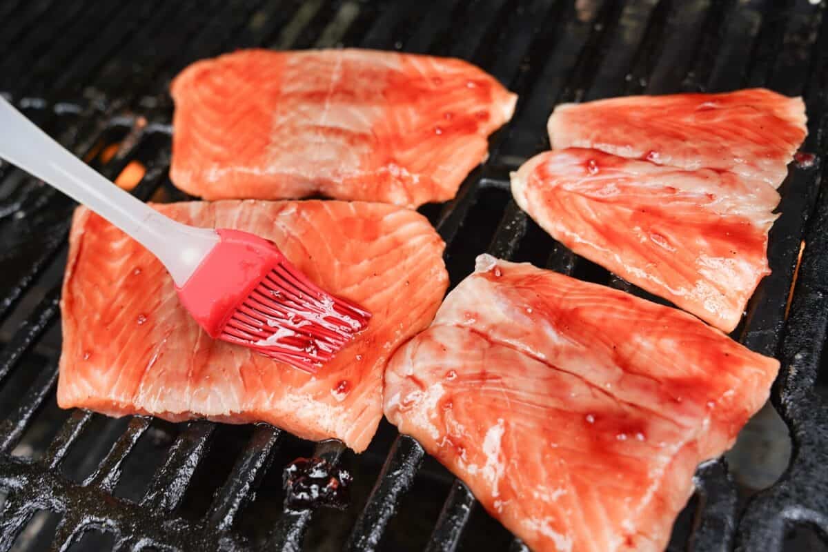 brush brushing on cherry glaze onto salmon fillets on the grill