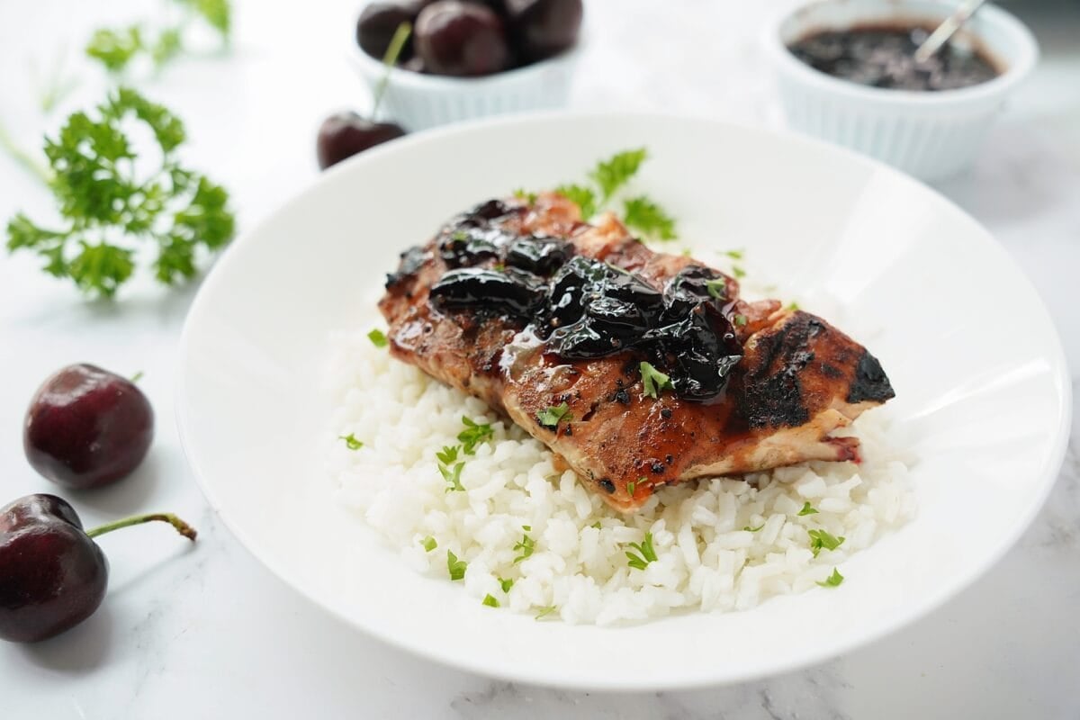 horizontal image of cherry glazed salmon plated over white rice in white bowl