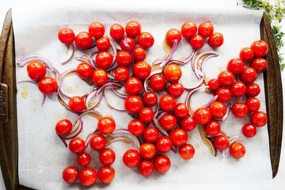 cherry tomatoes and sliced onions on baking sheet with parchment paper prior to baking