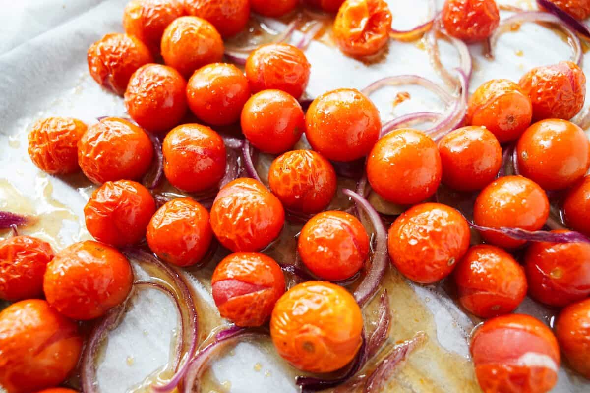 cherry tomatoes and sliced onions on baking sheet with parchment paper after baking