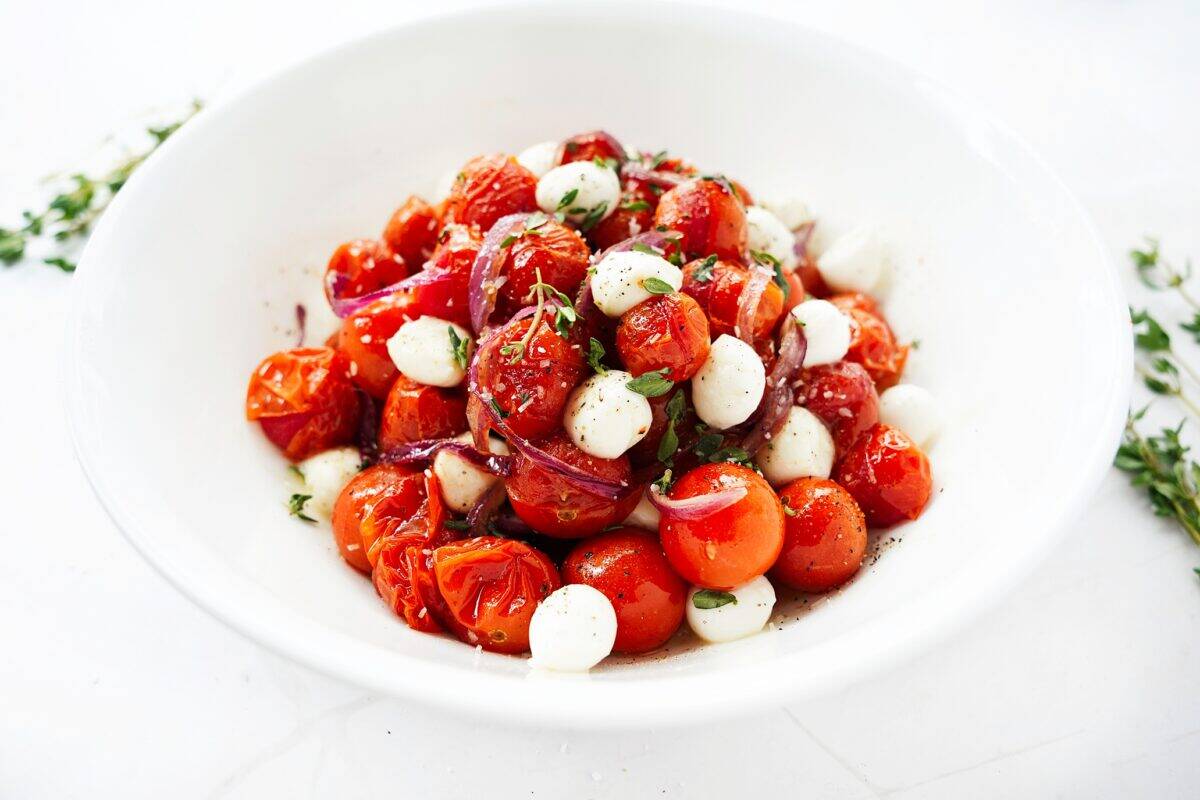 hot honey roasted onions and tomatoes in white bowl with mozzarella pearls and garnished with fresh thyme leaves