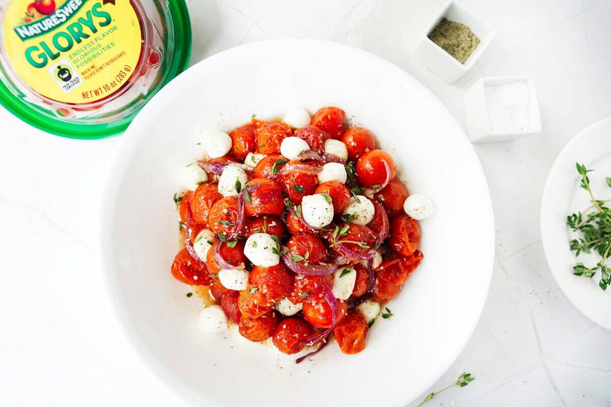 overhead shot of roasted hot honey cherry tomatoes and onions in white bowl topped with fresh mozzarella pearls and thyme with naturesweet glorys on the side