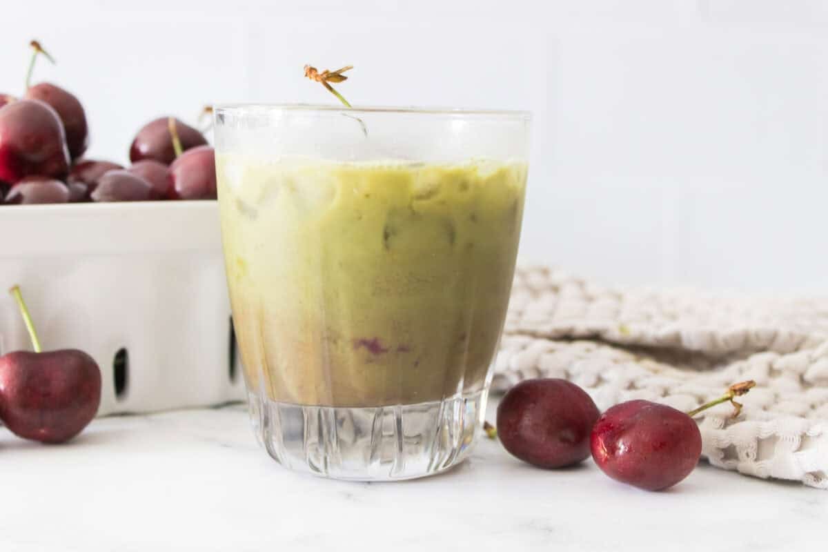 head on shot of cherry matcha latte with bowl of cherries in background