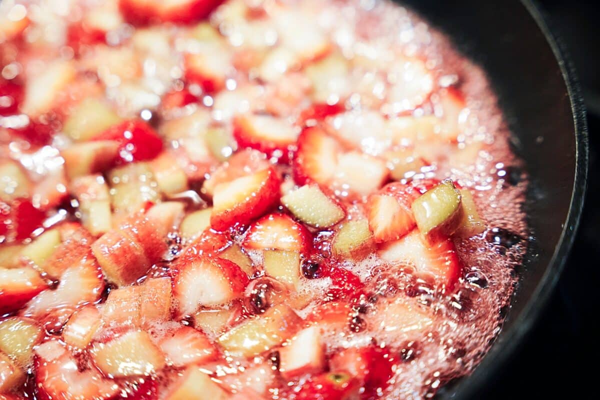 strawberries and rhubarb simmer in skillet with sugar, lemon juice and honey to thicken