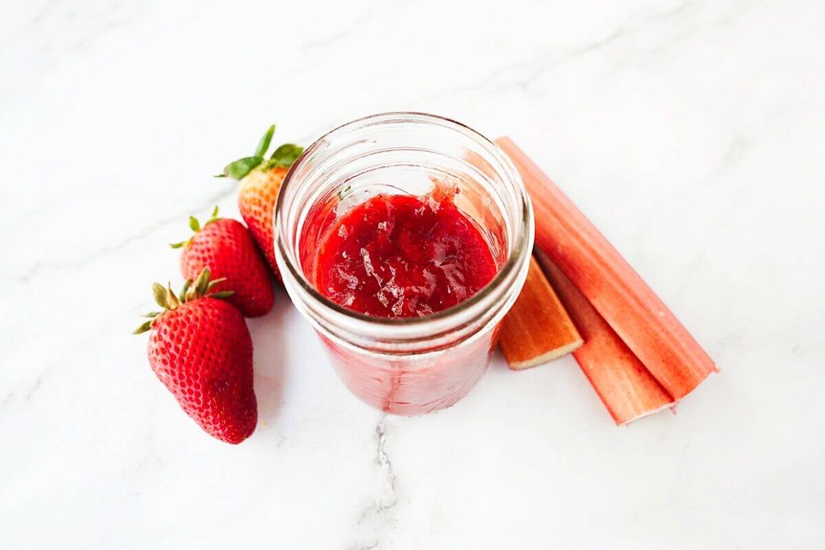 shot of strawberry rhubarb jam in mason jar with strawberries and stalks of rhubarb on the side