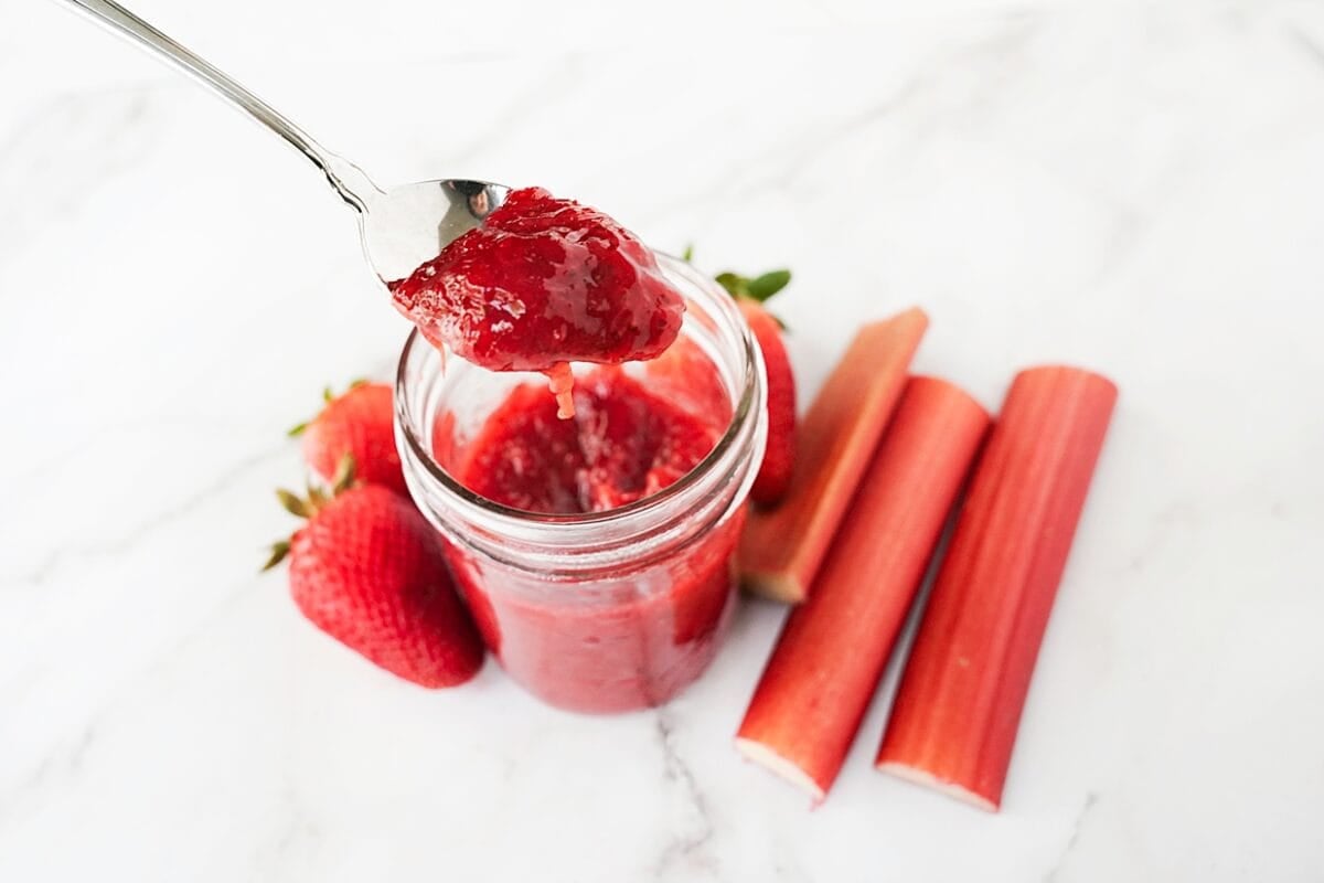 strawberry rhubarb jam on spoon over mason jar to show thickness