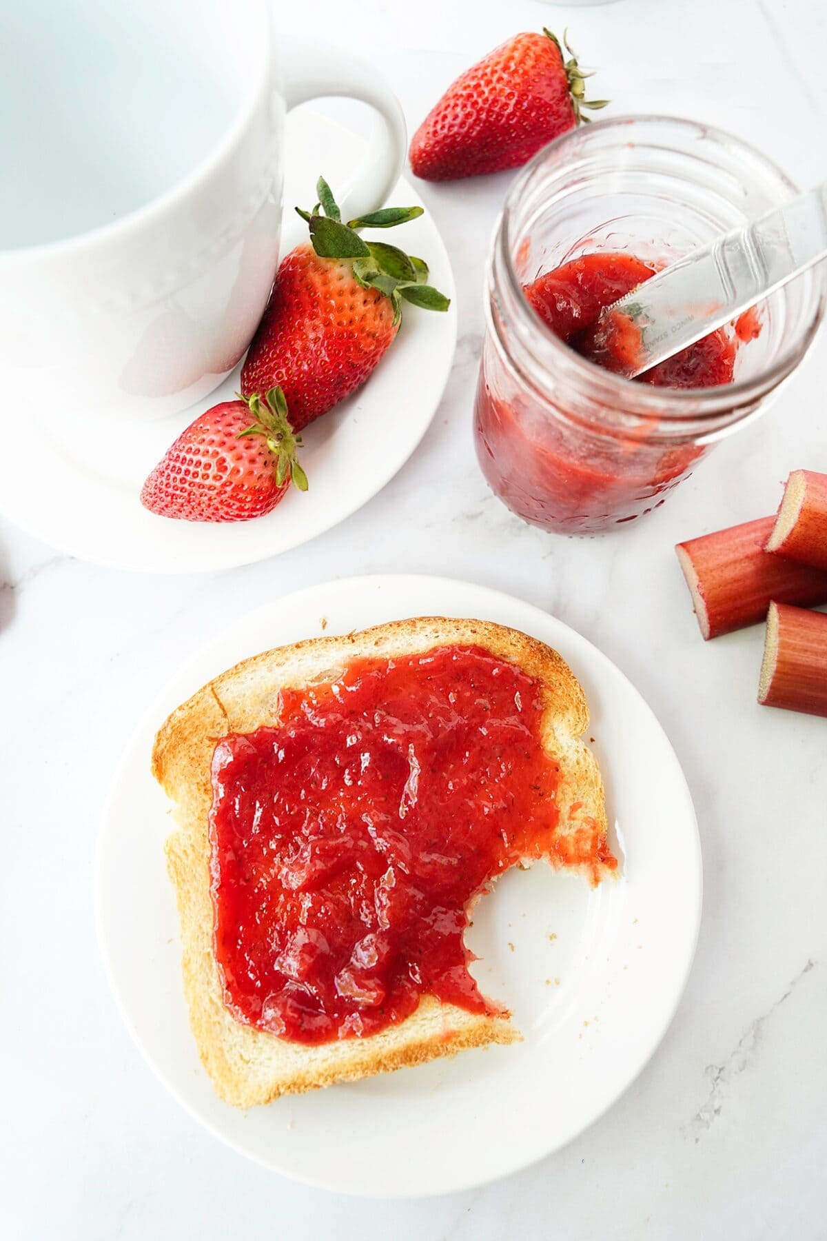 overhead shot of strawberry rhubarb jam on toast with some in mason jar with butter knife