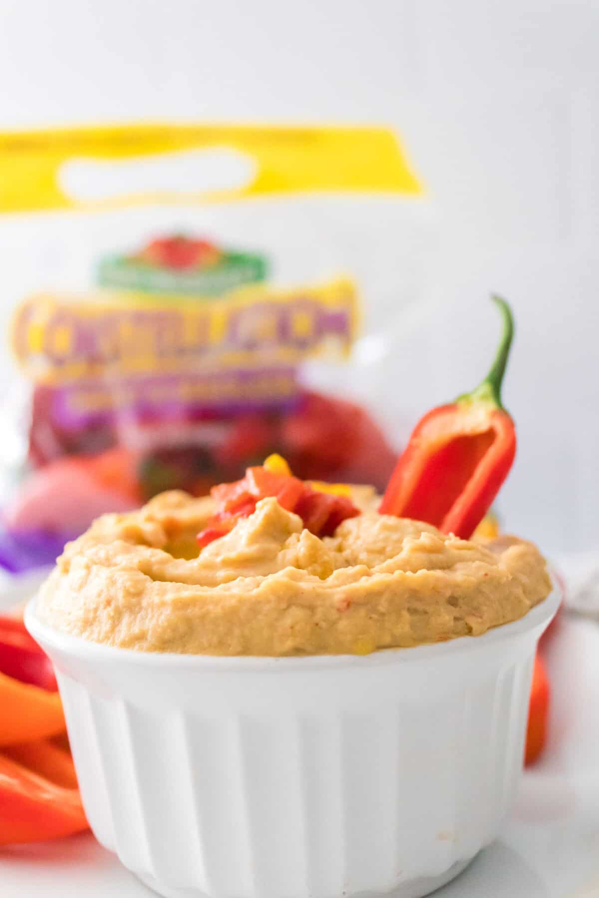 head on vertical shot of roasted pepper hummus garnished with roasted peppers with red mini pepper dipped in hummus