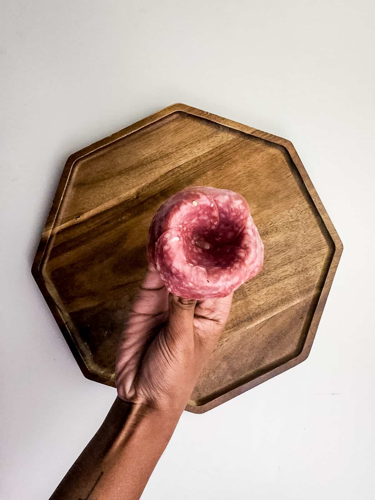 overhead shot of hand holding salami placed to look like a rose over cutting board