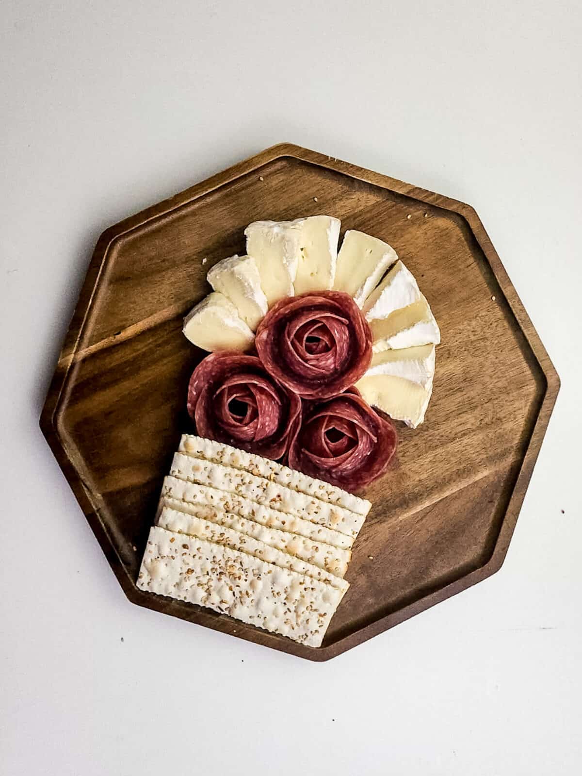 overhead shot of salami, crackers and brie cheese on cutting board